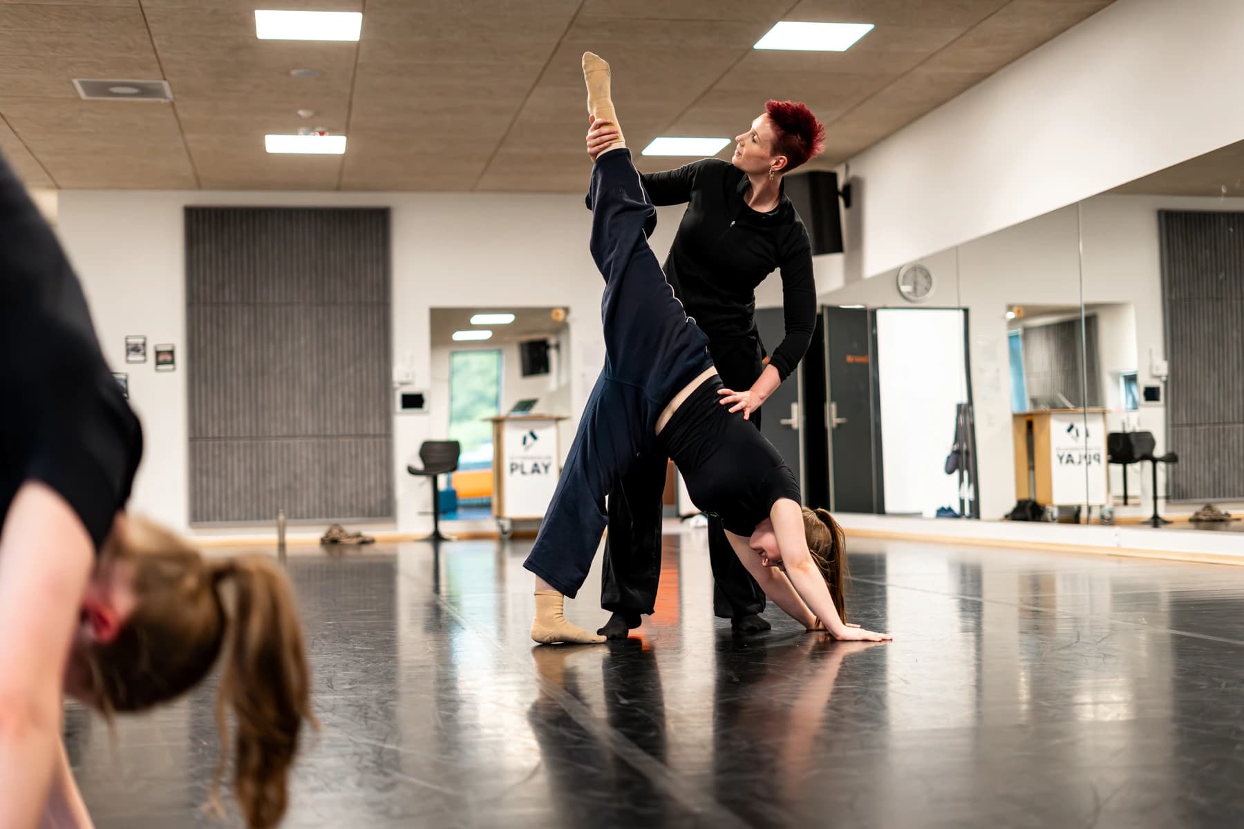 Instruktør hjælper danser med vertikal split i dansestudio med spejlvæg