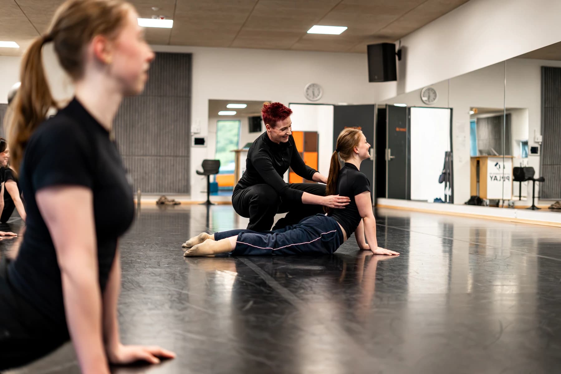 Instruktør hjælper ung danser med stræk på gulvet i dansestudio med spejlvæg